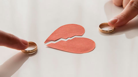 Two hands holding wedding rings next to a torn paper heart, symbolizing Rebuilding Your Home After Divorce.
