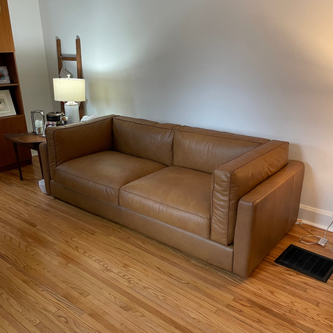 Brown leather sofa in a living room with wooden floor and white walls.