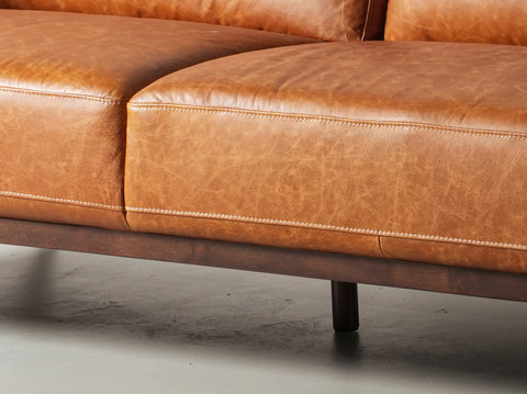 Close-up of Amore Cognac Distressed Leather 3 seater sofa showcasing full-aniline leather and tapered teak oak legs.