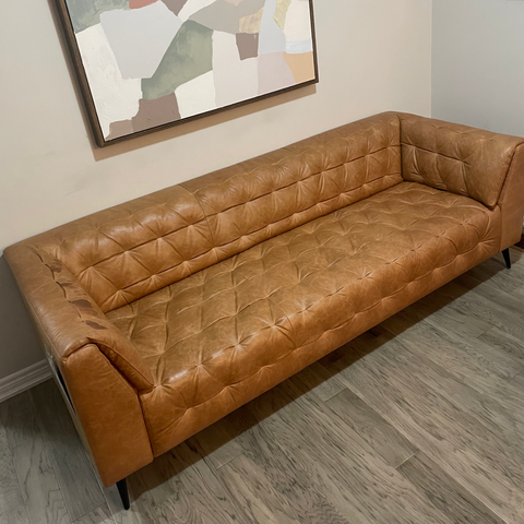 Brown leather sofa in a room with abstract art on the wall.