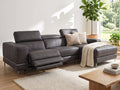 A dark gray leather sectional sofa with a chaise lounge and extended footrest, styled in a bright, modern living room with a wooden coffee table, textured rug, and potted plants.