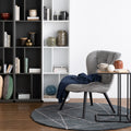 Modern living room with a stylish Amico Minimalist C-Shaped Laptop Table beside a grey chair, featuring bookshelves and decor.