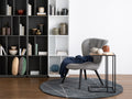 Modern living room with a stylish Amico Minimalist C-Shaped Laptop Table beside a grey chair, featuring bookshelves and decor.