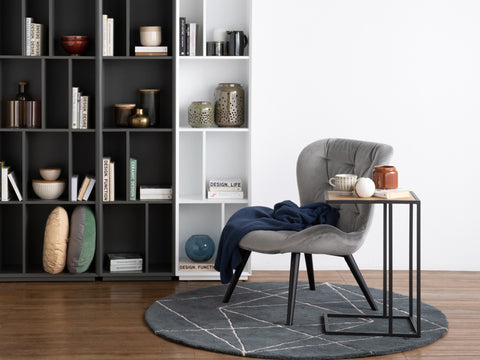 Modern living room with a stylish Amico Minimalist C-Shaped Laptop Table beside a grey chair, featuring bookshelves and decor.